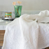 White Ines guest towel draped over a marble bathroom counter with green glass accessories in the background.