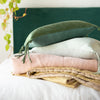 Ines Blanket | Ines throw blanket in rouge, folded and stacked with white, gold, and green tones - side view.