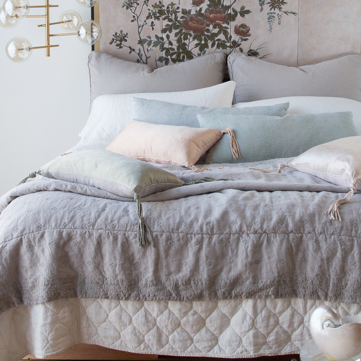 Ines Blanket | Ines throw blanket layered with mixed textures of charmeuse, quilted linen, and plain linen in soft grey, blue, pink and white tones - end of bed view.