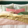 Ines Blanket | Ines throw blanket in rouge, layered under green, pink, and gold tones on a white bed, - cropped end of bed view.