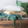 A stack of angled Taline throw pillows on a neatly folded blanket, highlightling hand-tied tassel detail - side view.