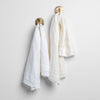 Austin Guest Towel | White | midweight linen guest towels in white and winter white on towel hooks mounted to a white wall.