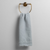 Austin Guest Towel | Cloud | midweight linen guest towel with raw edge band at both ends hanging from a towel ring mounted to a white wall.