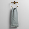 Austin Guest Towel | Eucalyptus | midweight linen guest towel with raw edge band at both ends hanging from a towel ring mounted to a white wall.
