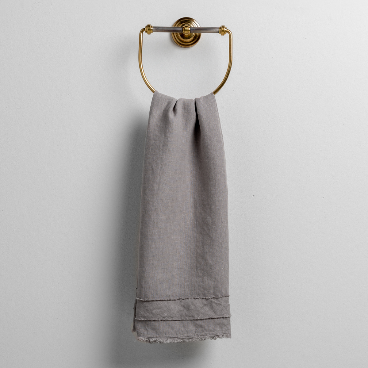 Austin Guest Towel | Fog | midweight linen guest towel with raw edge band at both ends hanging from a towel ring mounted to a white wall.