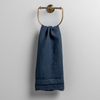 Austin Guest Towel | Midnight | midweight linen guest towel with raw edge band at both ends hanging from a towel ring mounted to a white wall.