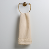 Austin Guest Towel | Parchment | midweight linen guest towel with raw edge band at both ends hanging from a towel ring mounted to a white wall.