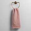 Austin Guest Towel | Rouge | midweight linen guest towel with raw edge band at both ends hanging from a towel ring mounted to a white wall.