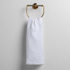 Austin Guest Towel | White | midweight linen guest towel with raw edge band at  both ends hanging from a towel ring mounted to a white wall.