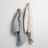 Austin Guest Towel | a pair of midweight linen guest towels in cloud and parchment on gold towel hooks mounted to a white wall.