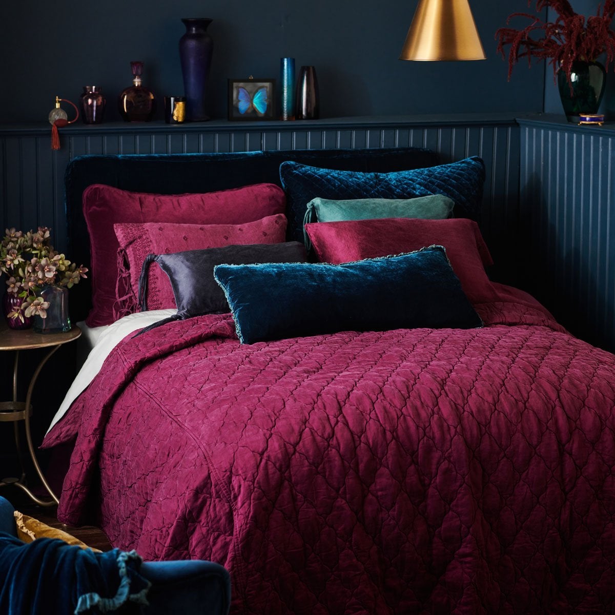 Carmen Throw Pillow | Carmen lumbar pillow in cenote, on a bed with deep fig and dark blue tones. Walls and art/accessories are a moody dark blue.