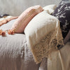 Frida Pillowcase (Single) | Frida pillowcase in parchment layered on a bed with moonlight and pearl tones in linen, cotton velvet, and silk velvet - side view.