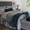 Bria Duvet Cover | Cotton sateen duvet cover in mineral shown with cotton sateen sheets and pillowcases in sterling with midweight linen shams and bed skirt in eucalyptus. A silk velvet quilted throw blanket and pillow are also on the bed shown from an angle.