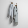 Mattine Guest Towel | cloud and eucalyptus linen guest towels with mattine lace hanging from decorative towel hooks against a plain white wall.