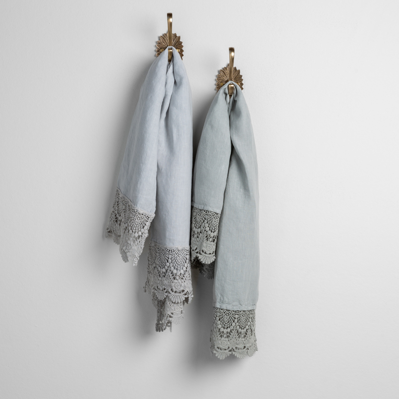 Mattine Guest Towel | cloud and eucalyptus linen guest towels with mattine lace hanging from decorative towel hooks against a plain white wall. 