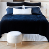 Silk velvet quilted shams and matching coverlet in deep midnight blue, layered simply with white and blue sleeping pillows and a white lumbar pillow - end of bed view.