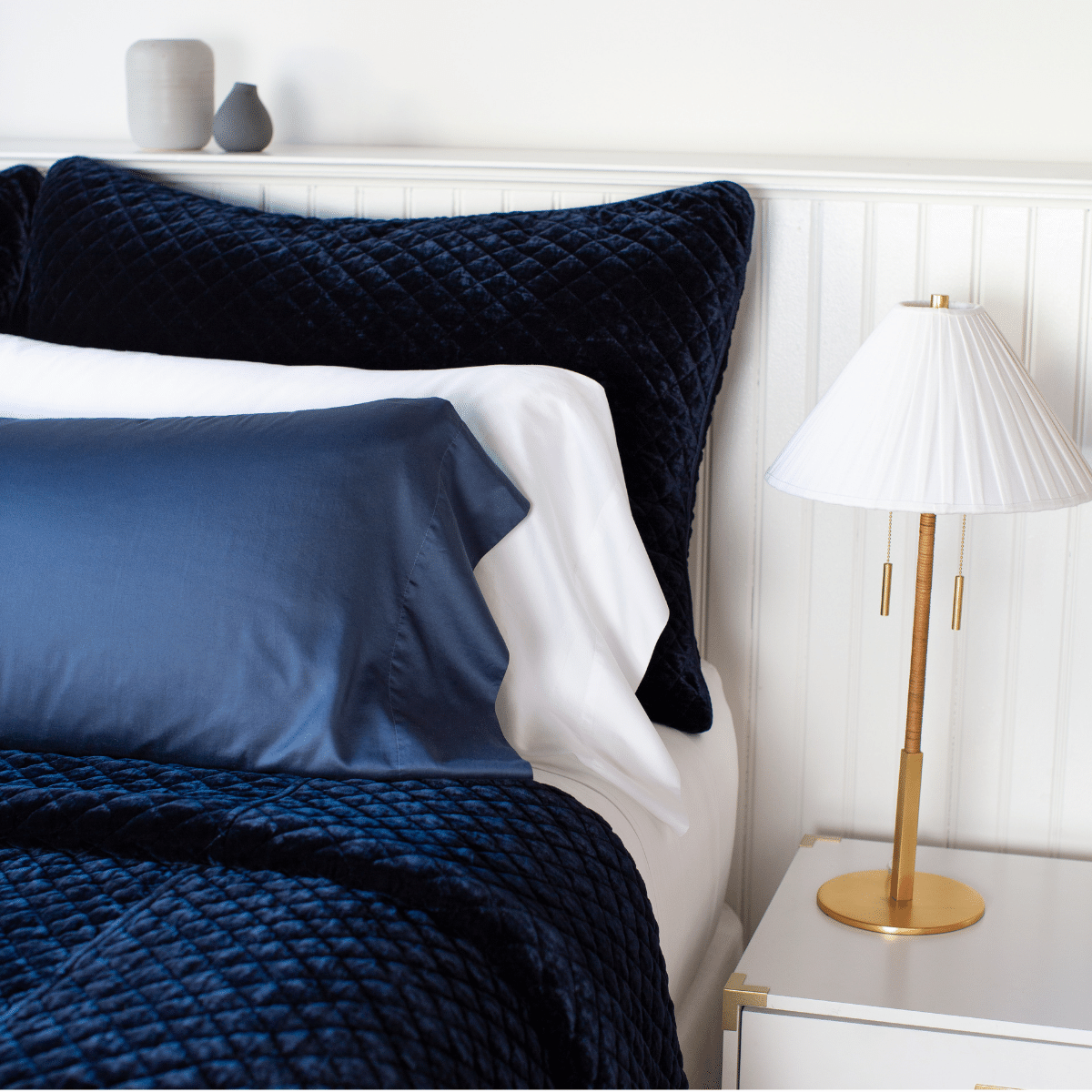 Midnight | Silk velvet quilted coverlet in deep midnight blue with matching shams, layered simply with white and midnight sleeping pillows - cropped three-quarter angle.