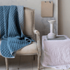 Silk Velvet Quilted Blanket | Silk velvet quilted throw blanket in cloud, draped over a light neutral antique couch. The blanket is rumpled, showing the satin back - cropped view.