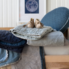 Luna Baby Blanket | Blankets in cloud and midnight folded and loosely stacked on a toddler bed with other blankets in varied textures and blue tones, and topped with beige baby booties.