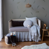 Linen Whisper Baby Blanket | Blanket in cloud, draped over the front of a crib in blue and grey tones, in nursery with warm wood tones and botanical tone on tone wall paper.