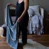 Carmen Baby Blanket | A pregnant woman, seen from the shoulders down, holding a blanket open in cloud in a blue and grey toned nursery.