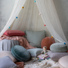 Linen Whisper Baby Blanket | Blankets in rouge and parchment rumpled among a canopy-covered nook on the floor covered witha cozy mix of pillows, blankets, books and a doll.