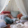 Silk Velvet Quilted Baby Blanket | Blanket in rouge folded and layered with many blankets and pillows in a cozy, canopy-covered reading nook.