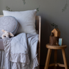 Linen Whisper Baby Blanket | Close up of blanket in cloud, draped over the front of a crib in other light blue and white tones, highlighting the ruffle trim.