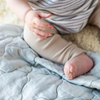 Luna Baby Blanket | Angled overhead close up view of rumpled blanket in cloud, shown with wooden toys and partial view of a sitting baby with bare feet.