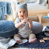 Luna Baby Blanket | Happy baby holding a wooden teether and sitting on rumpled blankets in cloud and midnight.