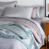 Cirillo shams stacked at the head of the bed with other sleeping pillows and throw pillows. A flat sheet with lace  is visible, pulled back over the duvet cover and coverlet - the throw blanket at the end of the bed is intentionally layered haphazardly to show satin binding detail against the quilt pattern.