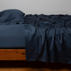 Bria Flat Sheet | Midnight | Cotton sateen flat sheet, shown with matching fitted sheet and sleeping pillow - side view.