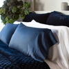 Bria Pillowcase (Single) | Bria pillowcases in white and midnight shown from three quarter close up angle. The cotton sateen shines against the deep blue silk velvet quilted shams and coverlet.