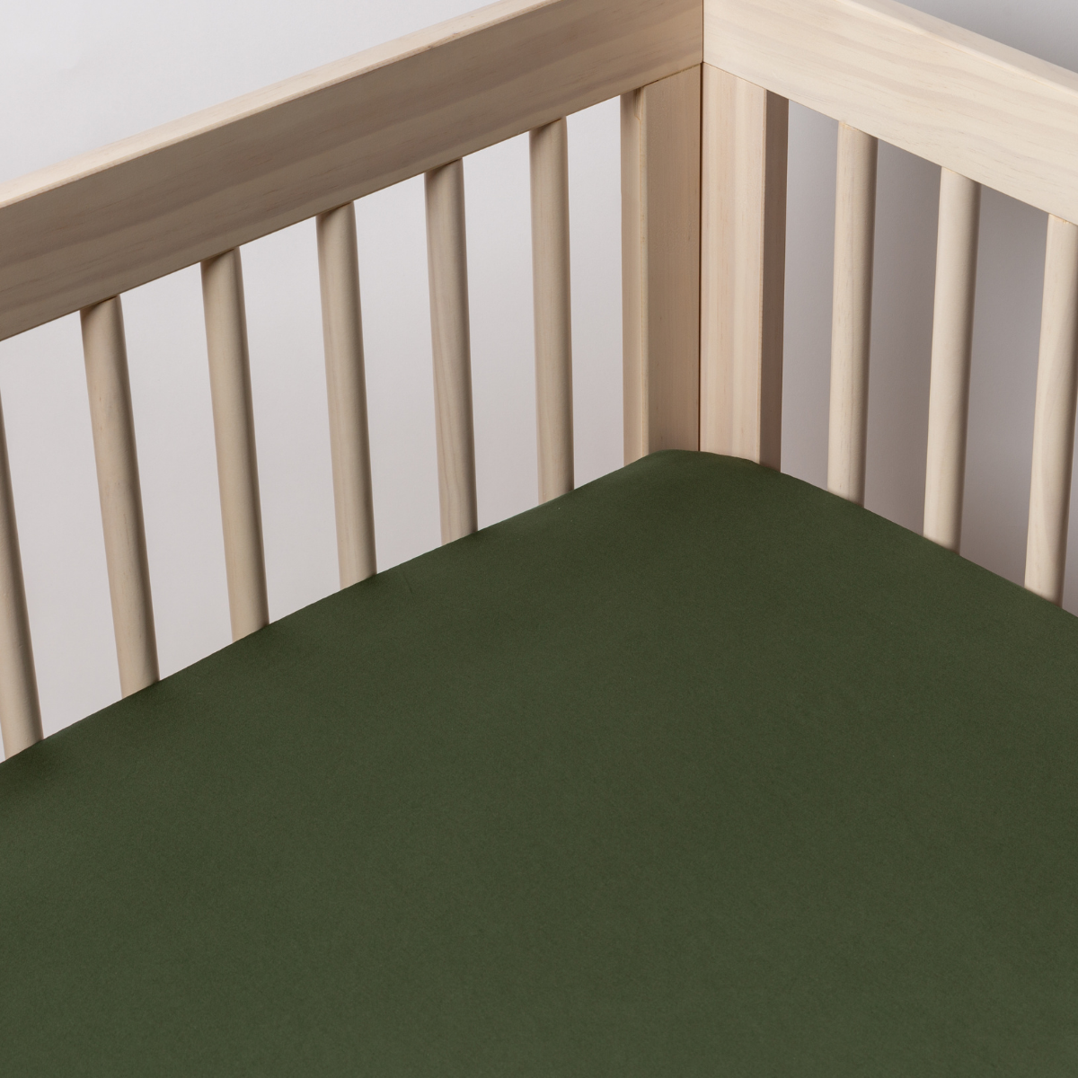 Bria Crib Sheet | Juniper | a cotton sateen crib sheet shot into the inside corner of a natural wood crib.
