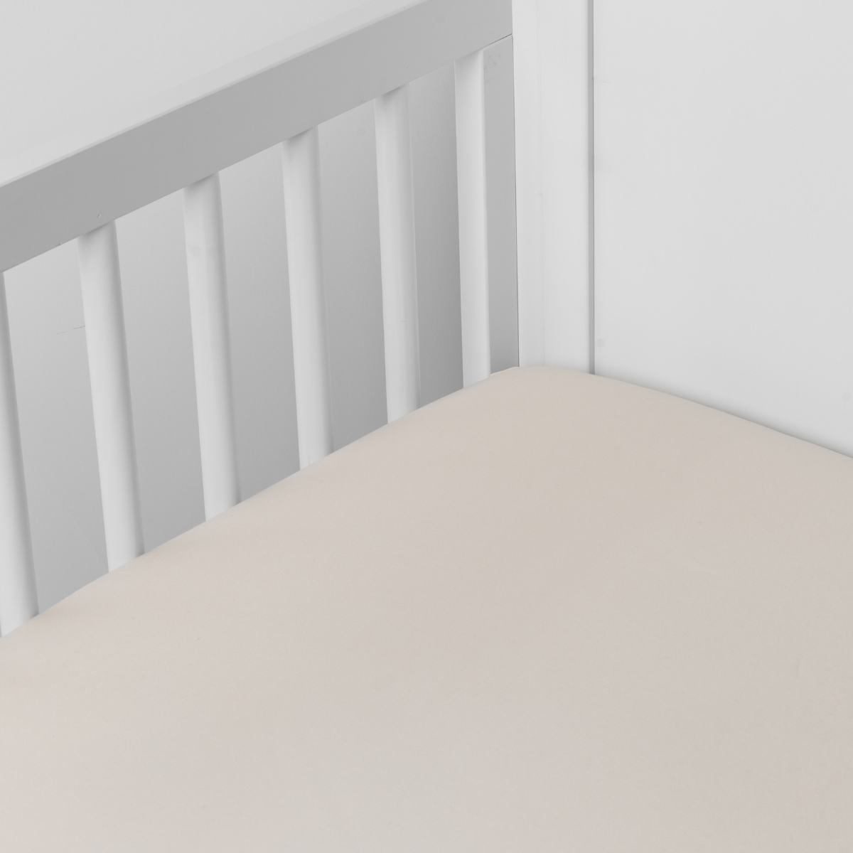 Bria Crib Sheet | Parchment | Cotton sateen crib sheet shown from a slight overhead angle into  an inside corner of a crib.