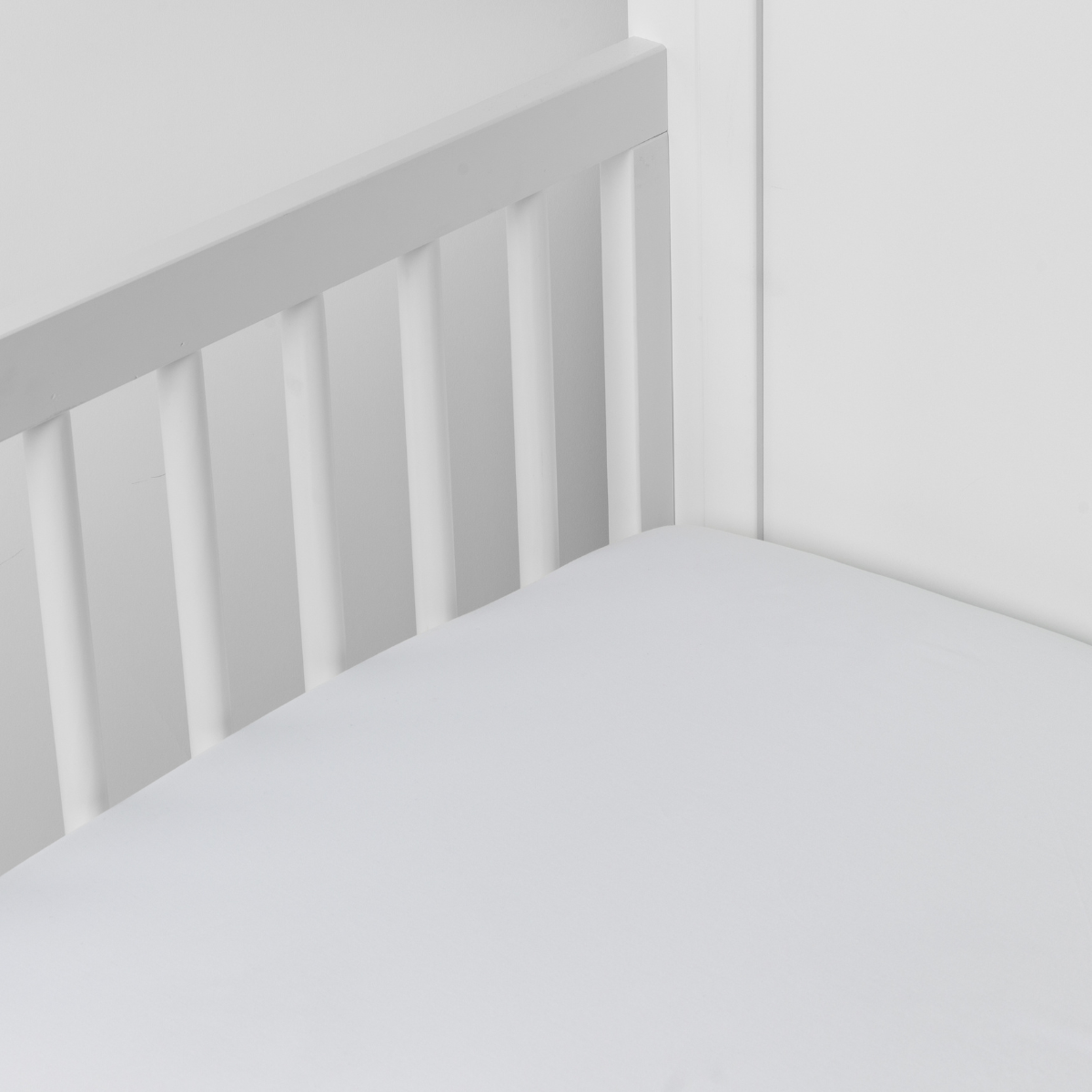 Bria Crib Sheet | White | Cotton sateen crib sheet shown from a slight overhead angle into  an inside corner of a crib.