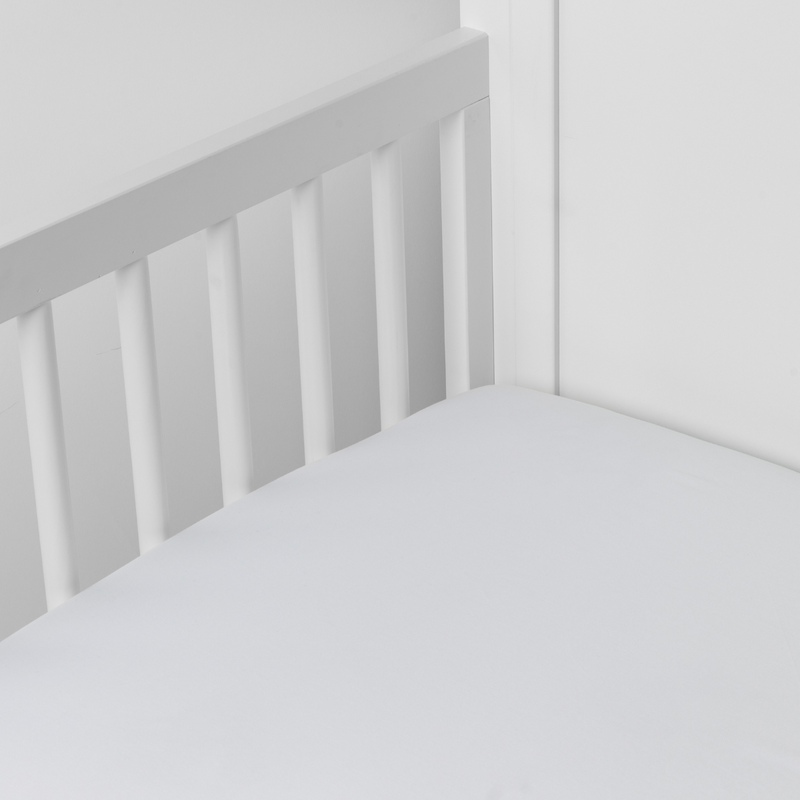 Bria Crib Sheet | White | Cotton sateen crib sheet shown from a slight overhead angle into  an inside corner of a crib.