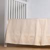 Bria Crib Skirt | Parchment | cotton sateen cribi skirt with a center pleat shown straight on from a slight angle in a crib without a crib mattress.