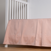 Bria Crib Skirt | Rouge | cotton sateen cribi skirt with a center pleat shown straight on from a slight angle in a crib without a crib mattress.