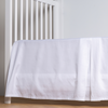 Bria Crib Skirt | White | cotton sateen crib skirt with a center pleat shown straight on from a slight angle in a crib without a crib mattress.