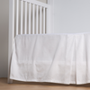 Bria Crib Skirt | Winter White | cotton sateen cribi skirt with a center pleat shown straight on from a slight angle in a crib without a crib mattress.