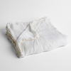 Carmen Baby Blanket | White | silk velvet baby blanket with charmeuse trim shown slightly overhead with a corner folded back to show trim detail against a white background.