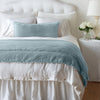 Carmen Throw Pillow | Cloud | Silk velvet lumbar pillow with petite ruffle and throw blanket shown on an all white, neatly made bed - foot of bed angle.