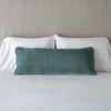 Carmen Throw Pillow | Eucalyptus | Silk velvet lumbar pillow with petite ruffle, leaning upright against neutral bedding and headboard.