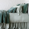 Carmen Throw Pillow | Eucalyptus | Silk velvet lumbar pillow with petite ruffle on a monochromatic, neatly made bed with matching accessory pieces - side view.