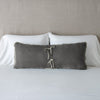 Carmen Throw Pillow | Carmen lumbar pillow in fog, leaning upright and backwards against neutral bedding and headboard, showcasing the silk charmeuse tie closures.