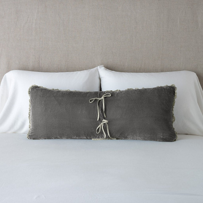 Carmen Throw Pillow | Carmen lumbar pillow in fog, leaning upright and backwards against neutral bedding and headboard, showcasing the silk charmeuse tie closures.