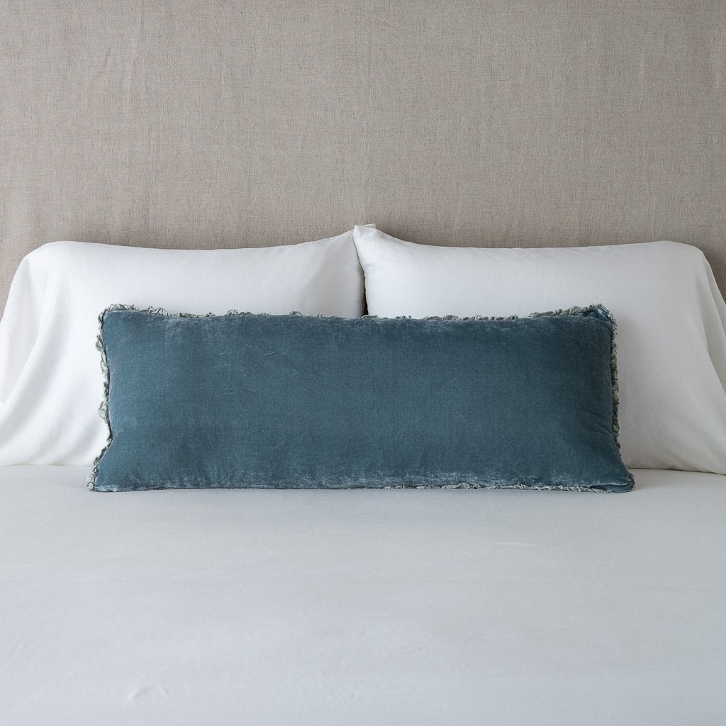 Carmen Throw Pillow | Mineral | Silk velvet lumbar pillow with petite ruffle, leaning upright against neutral bedding and headboard.