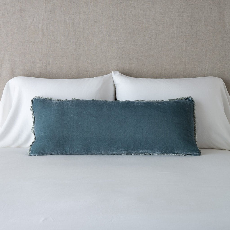 Carmen Throw Pillow | Mineral | Silk velvet lumbar pillow with petite ruffle, leaning upright against neutral bedding and headboard.
