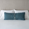 Carmen Throw Pillow | Mineral | Silk velvet lumbar pillow with petite ruffle leaning upright and backwards against neutral bedding and headboard, showcaseing the silk charmeuse tie closures.